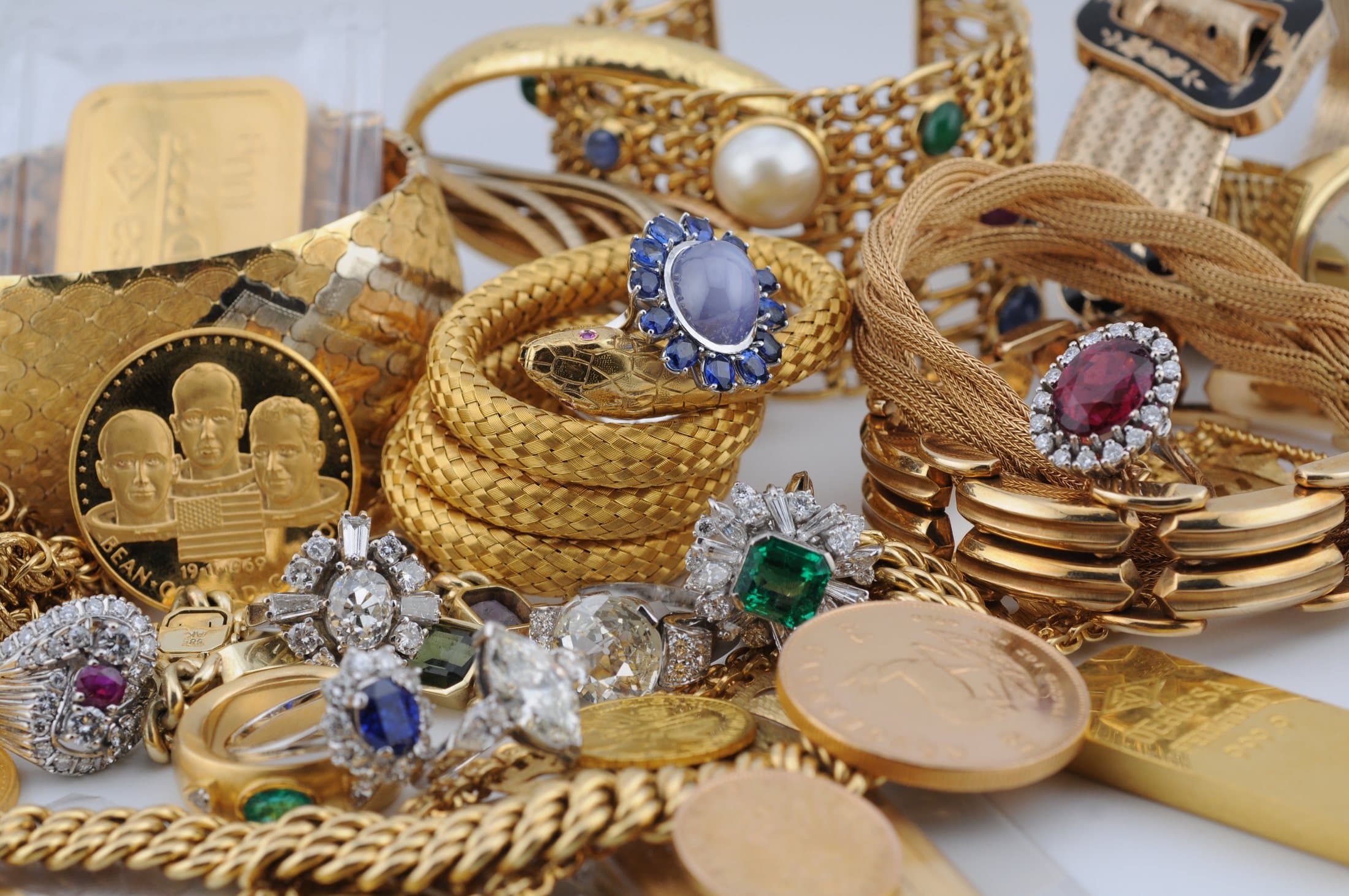 Goldschmuck mit Saphir-, Rubin- und Smaragdringen, dazwischen Goldmünzen